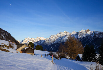 Fototapeta premium A snow-covered winter landscape with traditional wooden huts surrounded by towering peaks in the Swiss Alps.