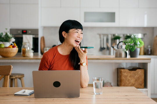 Smiling person working from home kitchen using laptop and voice mail