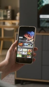 Vertical close-up of hand of anonymous man holding smartphone with dystopian sci-fi movie trailer on video streaming app, while eating chips, leisure and mobile entertainment concept