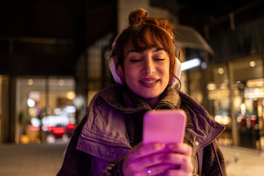 Woman with bangs wearing wireless headphones using smart phone