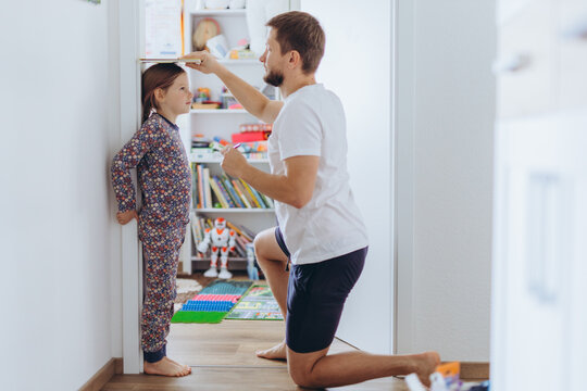 Father measuring daughter's height at home in the living room