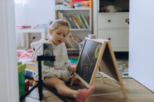 Child drawing creatively at home sitting by chalkboard and camera