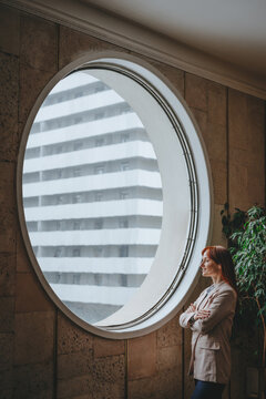 Businesswoman looking thoughtfully out a round window in modern office