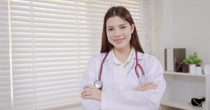 Asian female pediatrician in clinic office smiling warmly with folded arms, expressing professional confidence, medical expertise, and compassion in pediatric healthcare service slowmotion