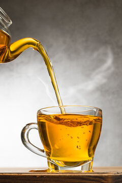 Glass cup of tea on wooden table with teapot filling.