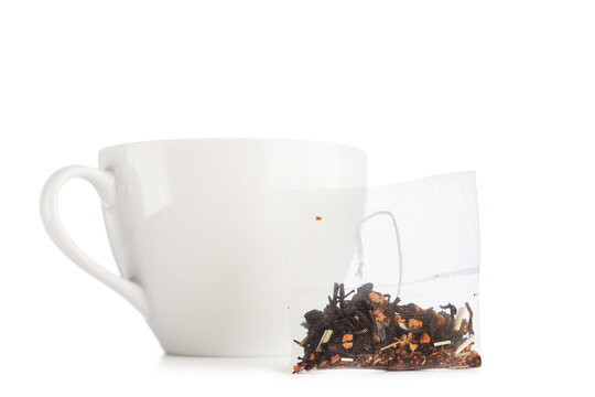Filter tea bag next to ceramic teacup, isolated on white background.