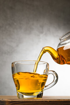 Glass cup of tea on wooden table with teapot filling.