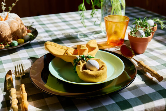 Easter table setting with folded napkin and pastel egg in rustic sunlight