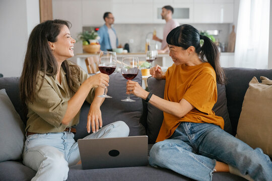 Friends laughing and enjoying wine together on the couch at home