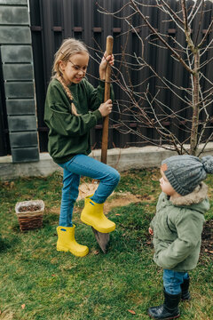 Kids digging soil and planting tree outdoors in yellow rain boots