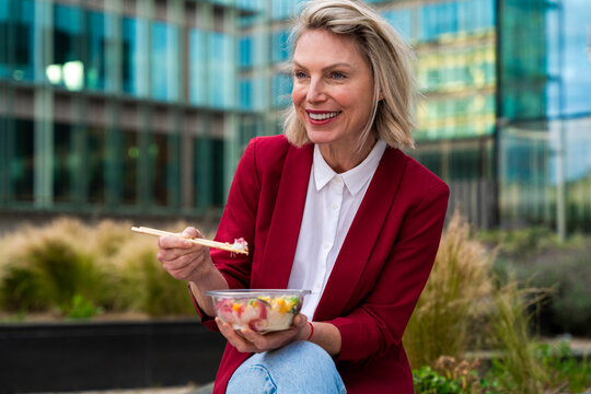 Businesswoman eating poke outdoors in urban setting