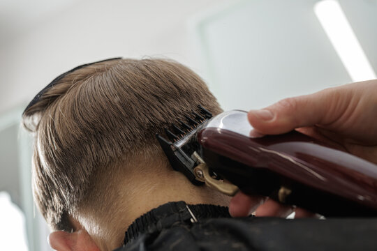 Hairdresser creating fade haircut with clipper on boy nape close up