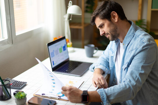 Businessman analyzing charts at desk with laptop in home office