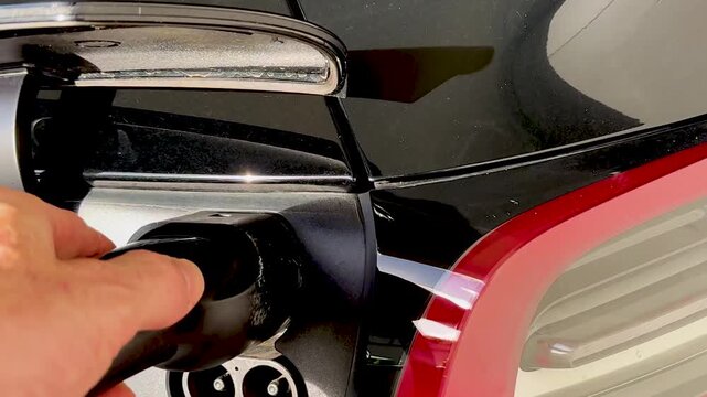 Close Up of Hand Plugging Charging Cable Into Electric Car Port