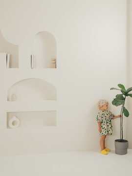 Girl child in a green dress and yellow shoes with a flower against a white wall with minimalist decor.