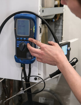 Technician adjusting digital measuring device on residential boiler, checking ambient carbon monoxide levels with probe sensor.