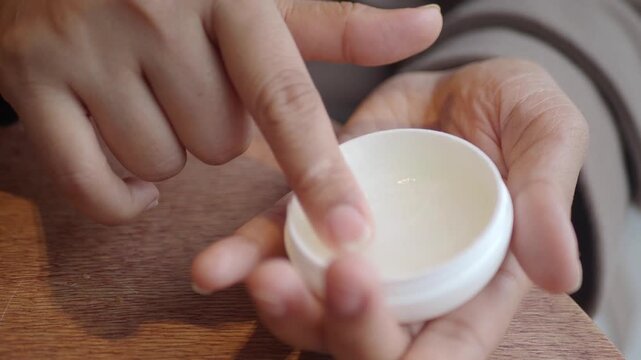 Woman finger taking moisturizing balm from small white container for daily skin care routine