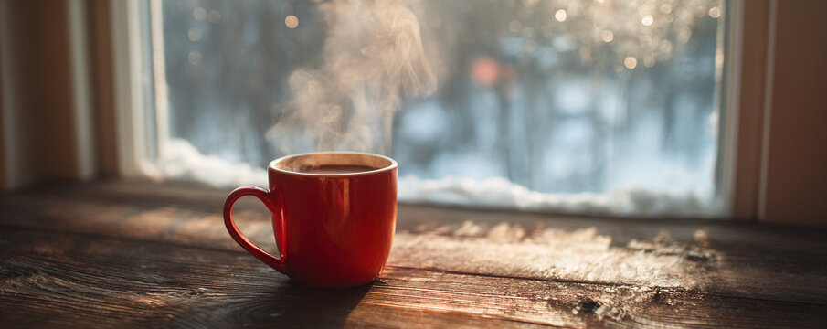 Red mug of hot chocolate steaming on wooden table, frosted window softly blurred in background 32k ultra HD