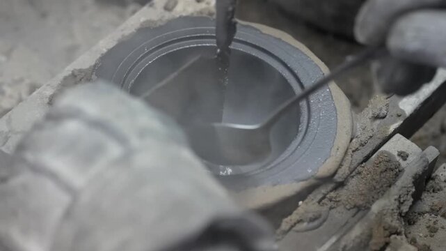Close up of steaming liquid metal or graphite being smoothed inside a mold with a spoon in a heavy industry setting