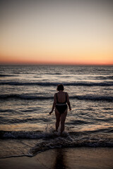 Fototapeta premium A girl is getting ready to go swimming and enjoying a beautiful sunset on the beach. Body positivity. Summer mood.