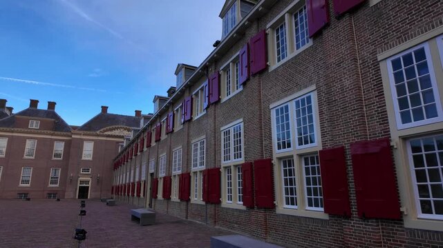 Exterior view of brick facade of Paleis Het Loo with traditional red shutters on windows. Historic Dutch Baroque architecture under blue sky during winter holiday season in Apeldoorn.