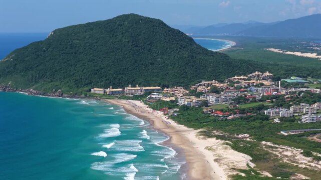 Aerial view of Praia do Santinho beach with waves rolling along coastline and Mirante do Santinho hillside, Santa Catarina, Brazil