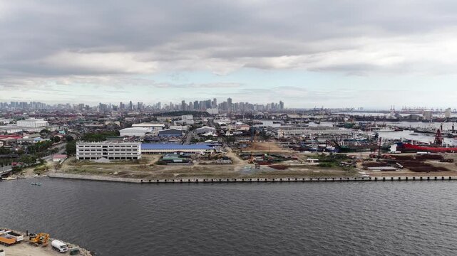 Expansive aerial perspective showing the industrial port area of manila with cargo ships and commercial buildings along the pasig river, revealing the sprawling urban cityscape against a cloudy sky