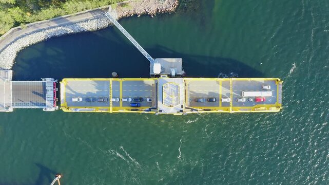 Yellow open deck island car ferry departing from a road loading ramp in Finnish archipelago. Aerial top down drone view.