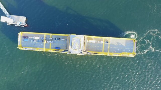 Yellow open deck island car ferry arriving to a road loading ramp in Finnish archipelago. Aerial top down view.