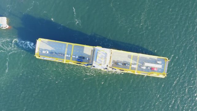 Yellow open deck island car ferry making way ahead in Finnish archipelago. Aerial top down view. Ferry partially loaded with vehicles.