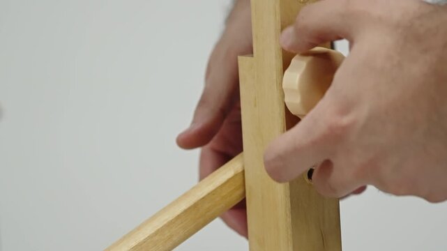 Close-up of hands tightening a wooden knob to secure a wood frame during simple furniture assembly, adjusting the brace and aligning dowel holes for a sturdy, stable structure.