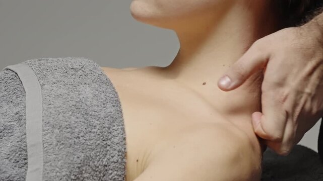 Close-up showing a relaxing neck and shoulder massage, with hands applying therapeutic pressure along the trapezius and nape as a client rests under a soft towel in a spa setting