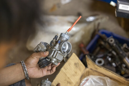 Mechanic hand holding motorcycle carburetor part during engine repair work showing focused attention to mechanical detail in dirty workshop setting