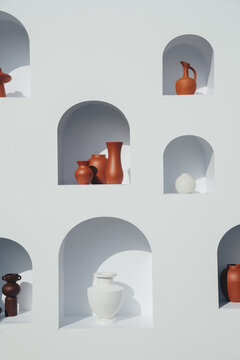 White and brown clay jugs on shelves on a white decorative wall. Graphic minimalism and shadows.