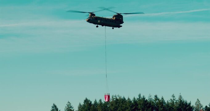 Transport helicopter of Dutch Royal Air Force carrying a water bucket for extinguishing wildfires in nature.
