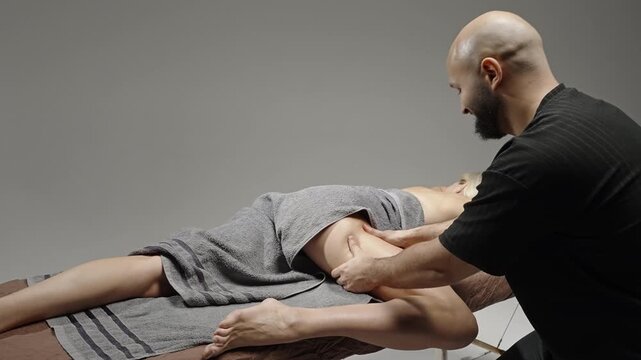 Professional deep tissue leg and glute massage therapy session with a therapist applying pressure and stretching techniques on a draped client in a quiet studio setting.