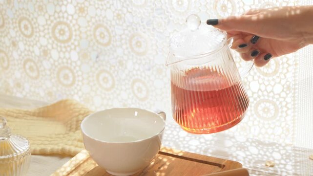 ティーポットから白いティーカップに紅茶を注ぐ女性の手元。ドリーショット