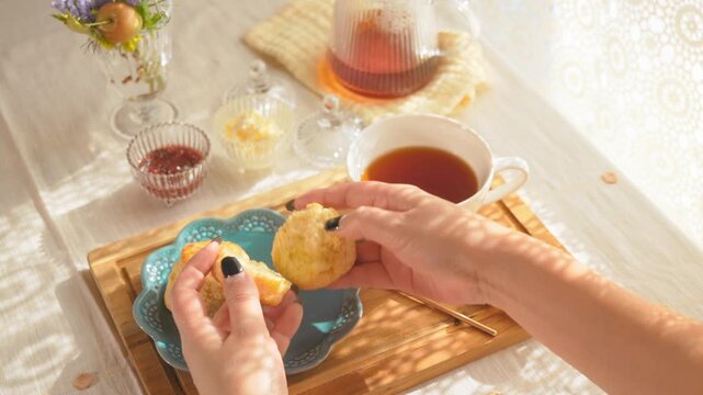 スコーンを割ってクリームやジャムを塗る女性の手元