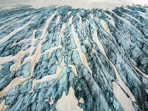 Aerial view of the textured glacier surface, etched with icy rivers and dusted with snow, shines with a cool blue hue, Obergoms, Valais, Switzerland.