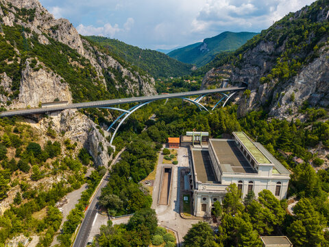 Aerial view of the soaring Ponte delle Marmore bridge gracefully meets rugged cliffs, with the power plant nestled below amidst lush greenery, Terni, Umbria, Italy.