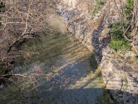Ruscello poco profondo che scorre tra rocce stratificate, con rami spogli sul bordo e acqua limpida in movimento