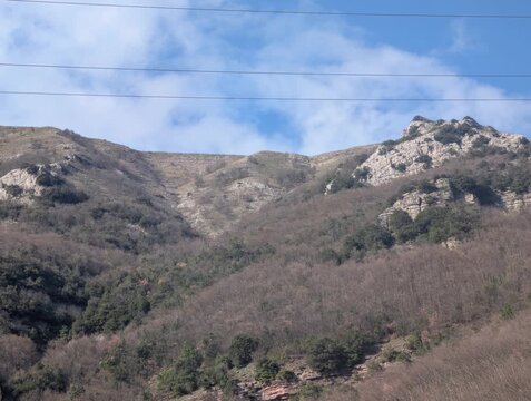 Paesaggio montano con pendii boscosi spogli, cielo parzialmente nuvoloso