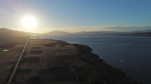 Aerial drone view of sunset light over Messolonghi Lagoon with calm water, farmland fields and long coastal shoreline landscape in western Greece