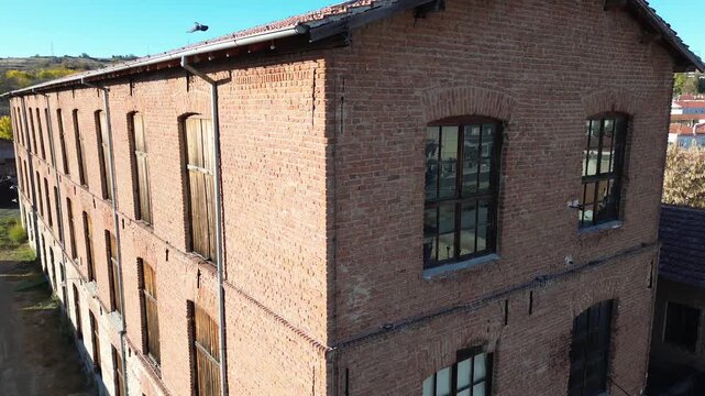 Cinematic close-up drone shot of the Tzivre silk factory facade. Detailed view of vintage red bricks, wooden shutters and old windows. Perfect for industrial history and architectural films.