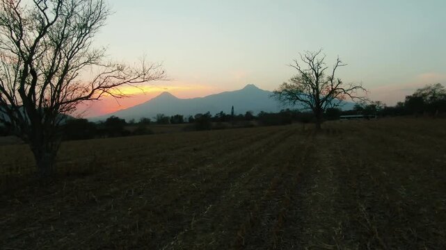Colima Volcanos at sunset with barren trees and fields in Jalisco, Mexico in aerial view