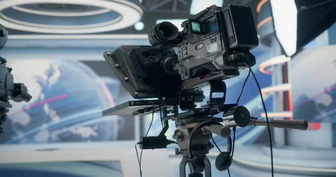 Backstage in a TV Station Production Room, a Broadcast Camera With Teleprompter Ready on the Studio Floor as Monitors, Ring Lights, World Graphics Frame Live News Technology