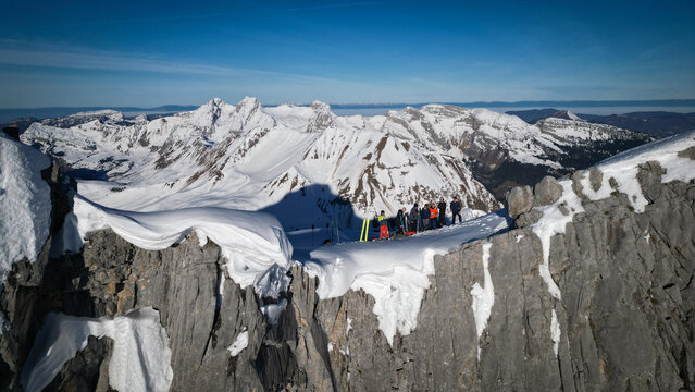 Aerial view of a group of people standing on Pointe de la Carmelite, their colorful ski gear a vibrant contrast against the stark white snow, Le Grand-Bornand, Auvergne-Rhone-Alpes, France.