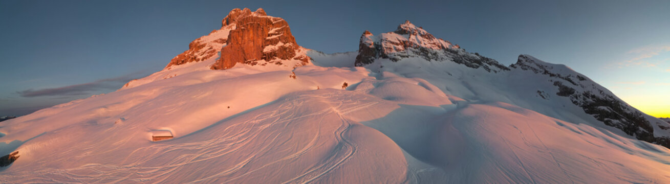 Panoramic aerial view of La Pointe Percee Aravis' Peak bathed in the warm glow of sunrise, ski tracks carving paths across the pristine slopes, Le Grand-Bornand, Auvergne-Rhone-Alpes, France.