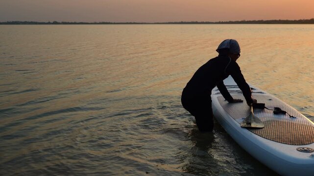 The silhouette of a person carrying a paddle board and playing at sunset symbolizes outdoor exercise, water sports, summer activities, a healthy lifestyle, and adventure travel.