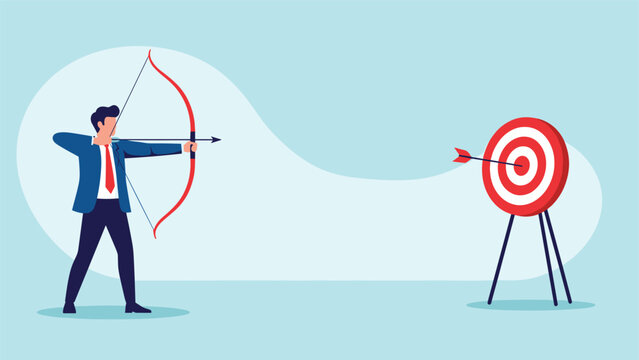 Determined businessman shooting an arrow with a red bow hitting the bullseye of a target to represent successful goal achievement.